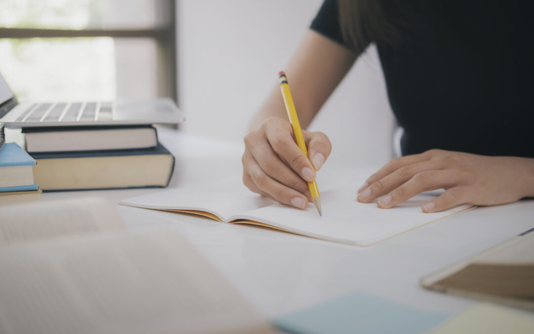 Photo of lady taking notes with a laptop and books nearby