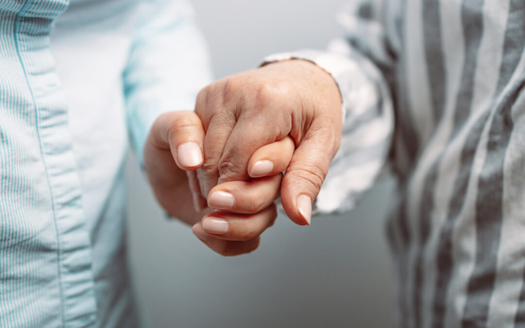Caregiver holding elders hand in hospice care background, closeup.
